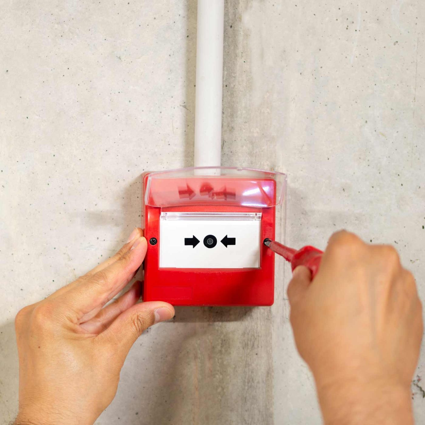 NCCS Group - A fire safety engineer installing a fire alarm on a cement wall.