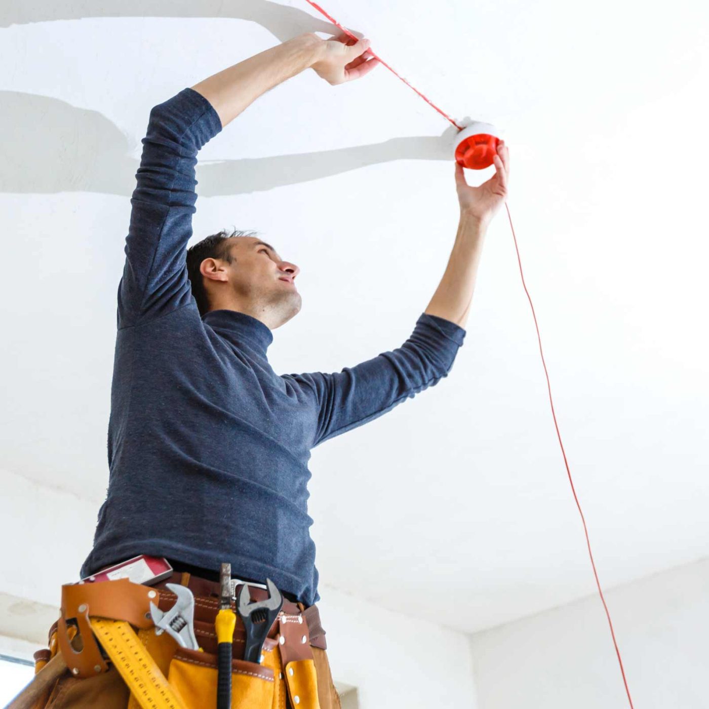 NCCS Group - A fire safety engineer installing a fire alarm in the ceiling.