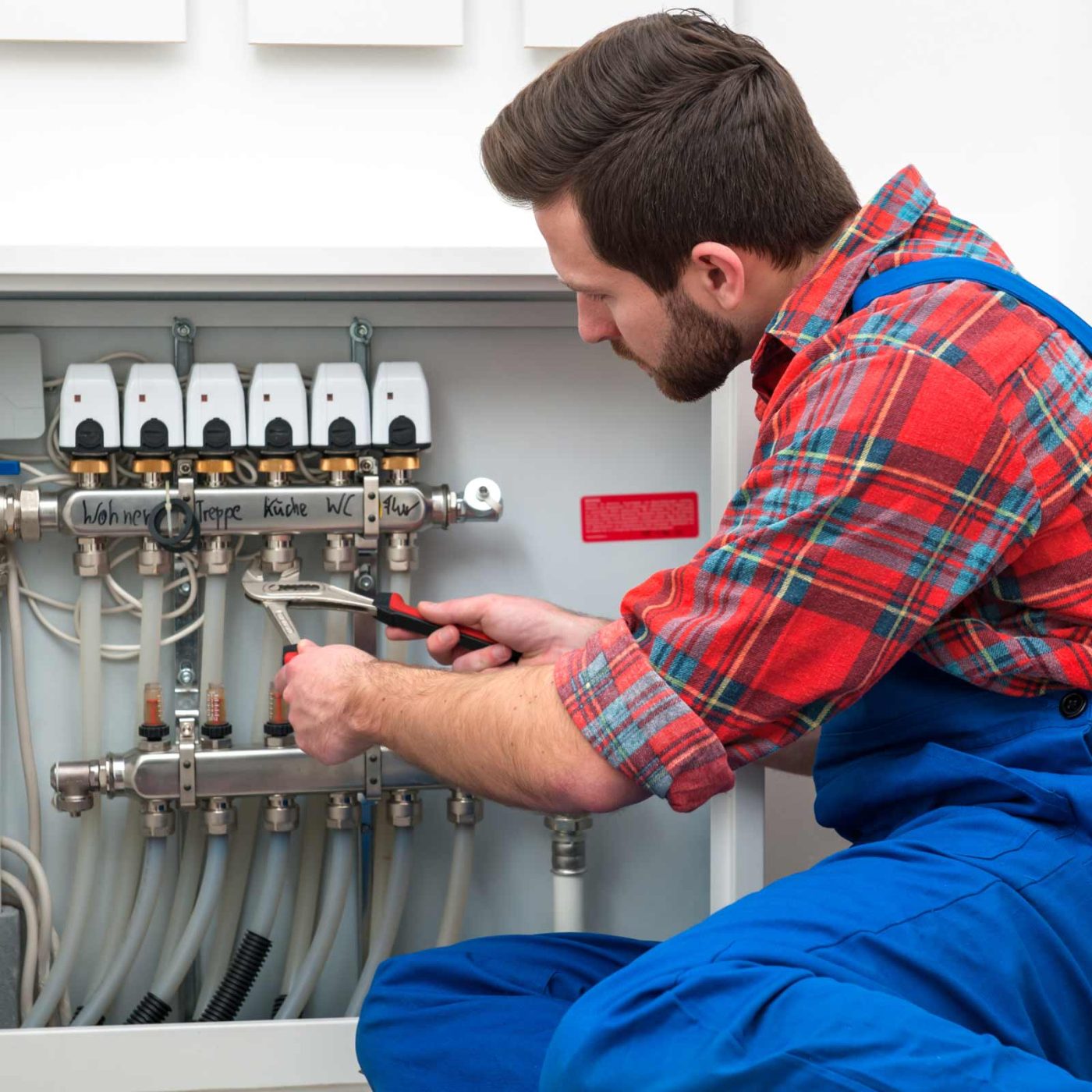 NCCS Group - A heating engineer crouched, repairing heating and pipes.